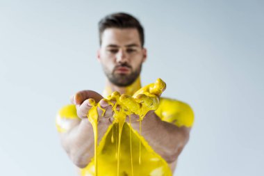 Handsome bearded man showing hands covered in yellow paint isolated on white background clipart