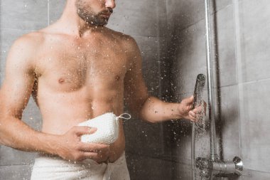 Handsome bearded man holding sponge behind shower glass clipart