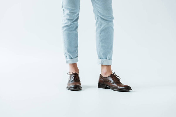 Cropped view of male legs in oxford shoes and jeans on white background