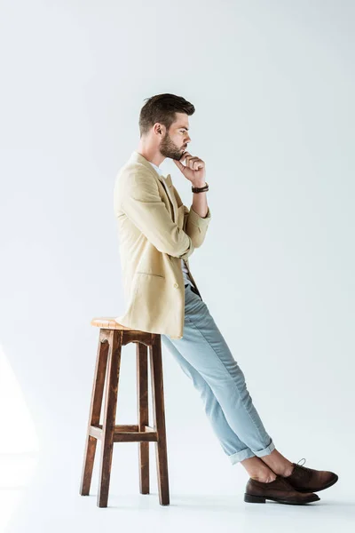 时尚的年轻男子坐在凳子上的白色背景下思考 — 图库照片