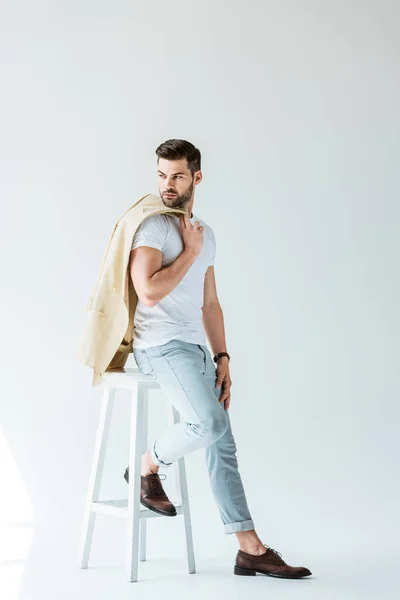 Elegante Jovem Segurando Jaqueta Sentado Banquinho Fundo Branco — Fotografia de Stock