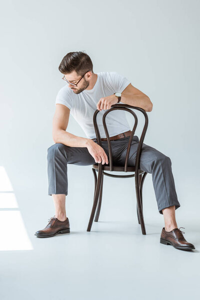 Fashionable confident man in glasses sitting on chair on white background