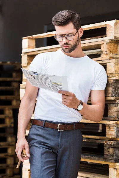 Stilvoller Junger Geschäftsmann Liest Geschäftszeitung Und Hält Zigarre Holzpaletten — kostenloses Stockfoto