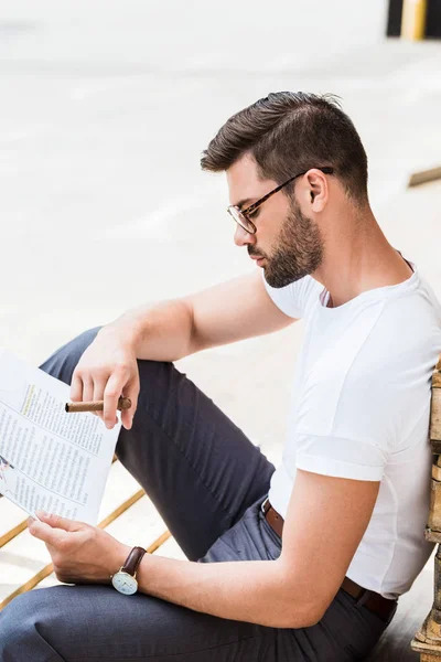 Stylish Young Businessman Reading Business Document Smoking Wooden Palettes — Free Stock Photo