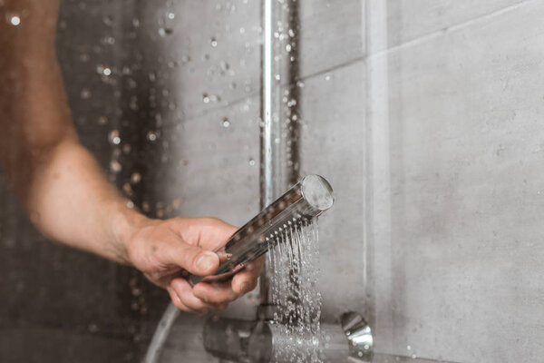 Cropped view of male hand holding shower behind glass