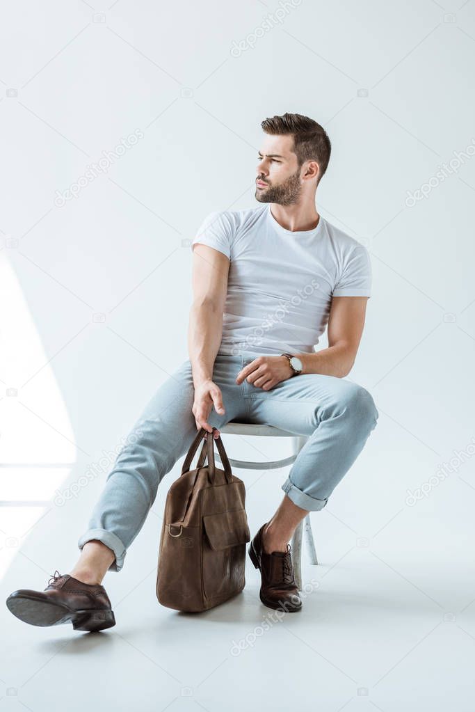 Stylish young man sitting on chair and holding briefcase on white background