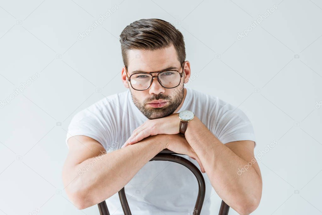Stylish young man in glasses sitting on chair isolated on white background