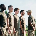 Boční pohled na africké americké taktické instruktor v sluneční brýle a mladé mnohonárodnostní vojáků na rozsah