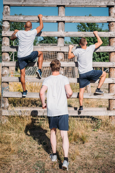 back view of multicultural soldiers practicing obstacle run on range on summer day