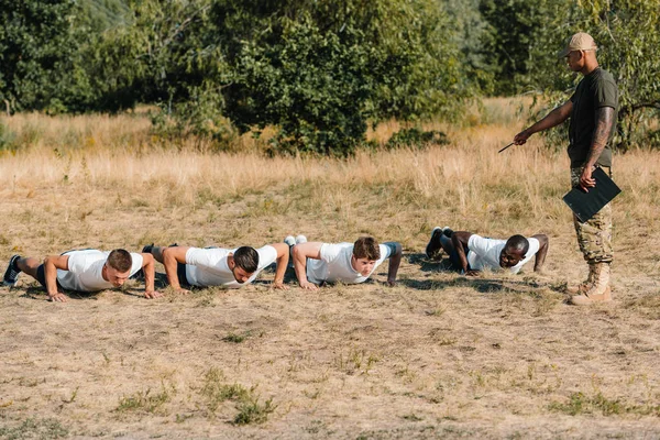 Tactical Instructor Notepad Examining Multicultural Soldiers Doing Push Ups Range — Free Stock Photo