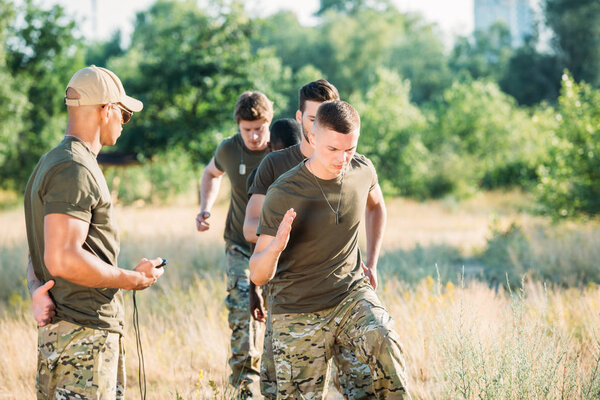 tactical instructor with stop watch examining multiracial soldiers during obstacle run on range