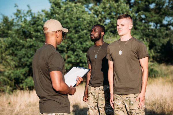 african american tactical instructor with notepad and young multiracial soldiers in military uniform on range