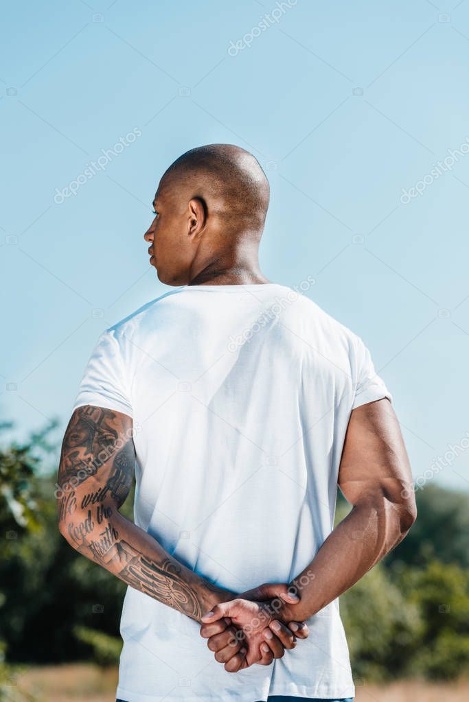 back view of african american tattooed soldier in white shirt against blue sky