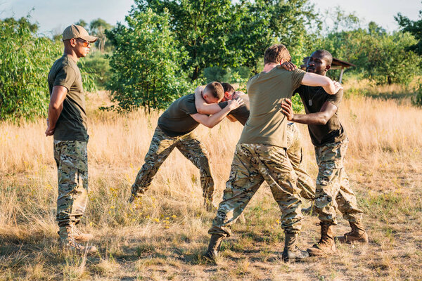 multiracial soldiers in military uniform practicing hand to hand fighting on range