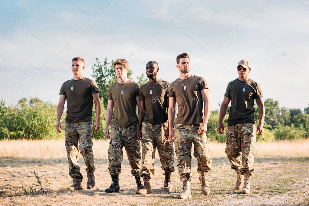 interracial soldiers in military uniform with tag dogs walking on range on summer day