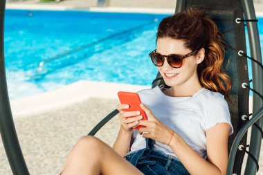 mutlu genç kadın önünde yüzme havuzu güneşlenme dinlenirken Smartphone kullanarak