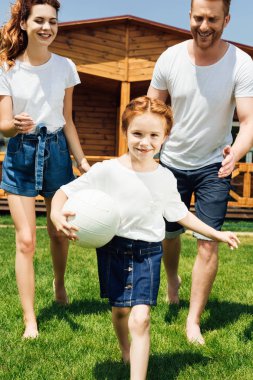 sevimli küçük kız voleybol topu tutarak ve anne-babadan çalıştıran