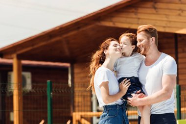 beautiful young family embracing in front of wooden cottage clipart