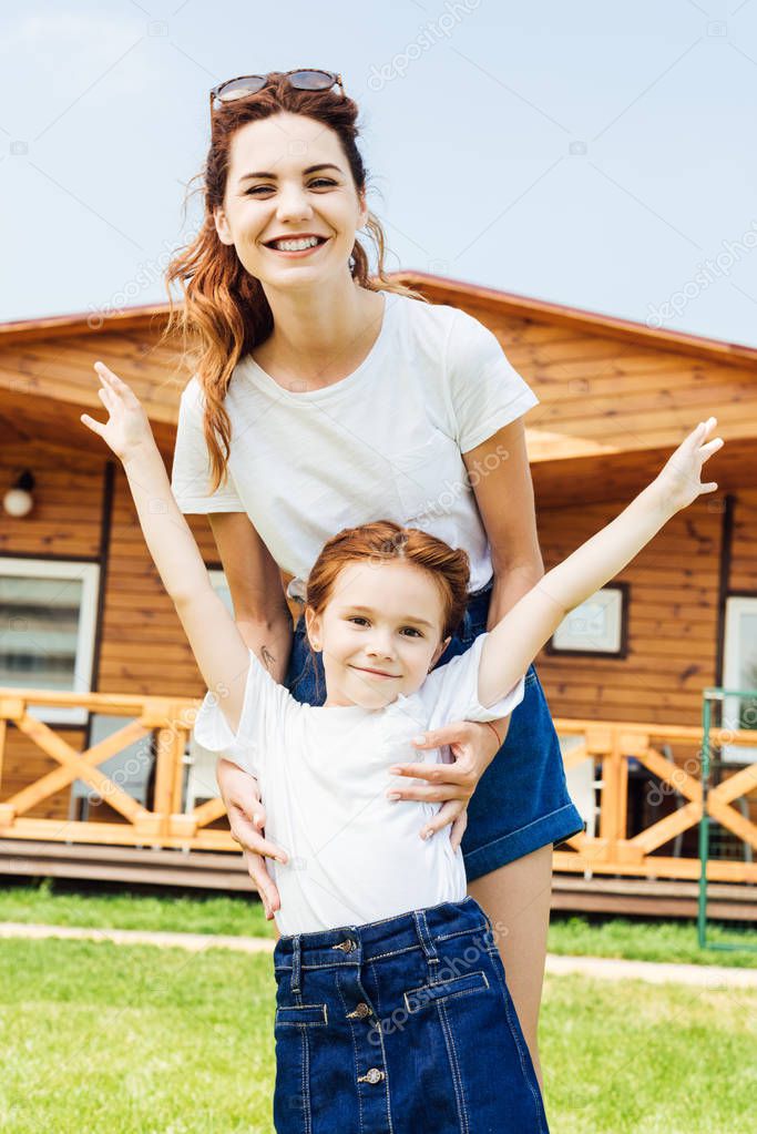 mother and daughter in white t-shirts in front of wooden cottage