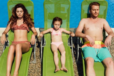 relaxed young family tanning on sun loungers together clipart