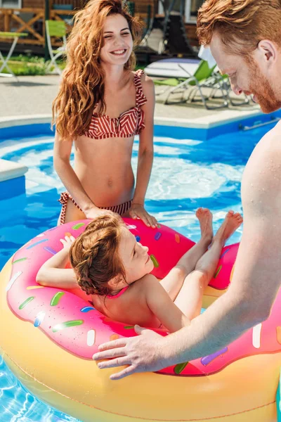 スイミング プールでのゴム輪に浮かぶ彼女の娘と一緒に過ごす幸せな若い親 — ストック写真