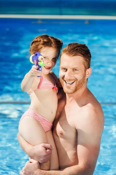 Gelukkig Vader Dochter Met Waterpistool Omarmen Zwembad Camera Kijken — Stockfoto