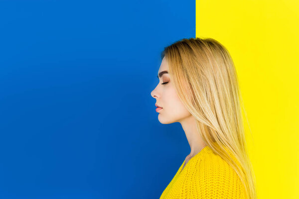 Portrait of girl with closed eyes wearing yellow clothes isolated on blue and yellow background