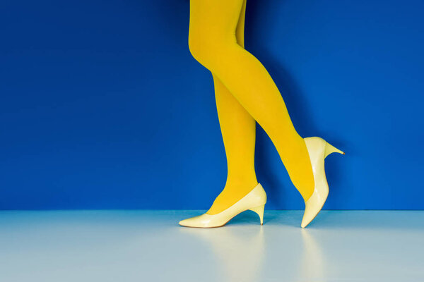 Cropped view of girl in yellow shoes and pantyhose on blue background