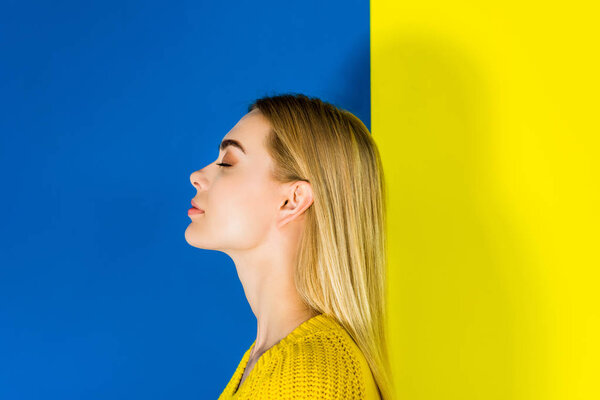 Portrait of blonde girl with closed eyes on blue and yellow background