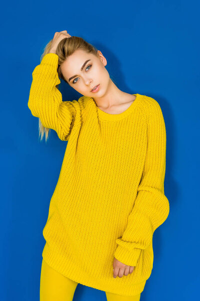 Elegant blonde woman in yellow sweater posing on blue background