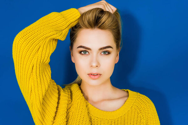 Female fashion model in yellow sweater posing on blue background
