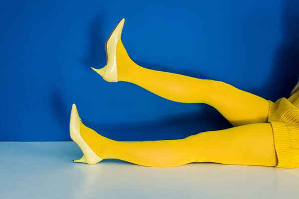 Cropped view of female legs in yellow shoes and pantyhose on blue background