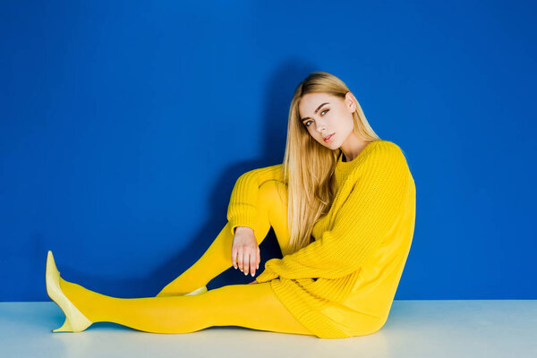 Female fashion model dressed in yellow sitting on floor on blue background