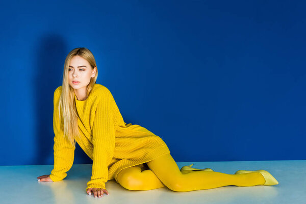Seductive young girl in yellow fashion clothes lying on blue background