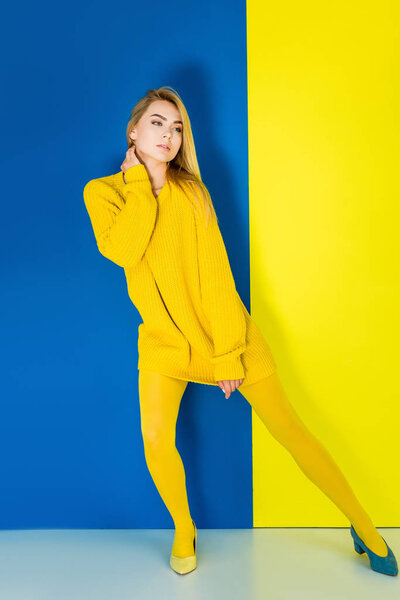 Female fashion model in yellow clothes and one blue shoe on blue and yellow background