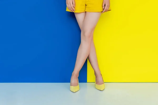 黄色鞋中女性腿的裁剪视图蓝色和黄色背景 — 图库照片