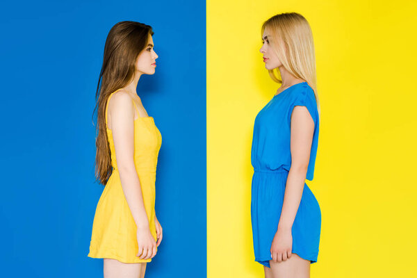 Female fashion models looking at each other isolated on blue and yellow background