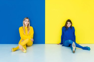 Mavi ve sarı zemin üzerine katta oturan moda kızlar