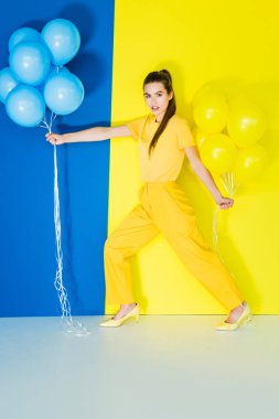 Balonlar mavi ve sarı zemin üzerine her iki elinde tutan çekici genç kız