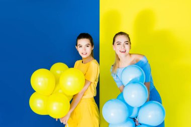 Gülümseyen ve parti balonu mavi ve sarı zemin üzerine tutarak zarif şık kadın