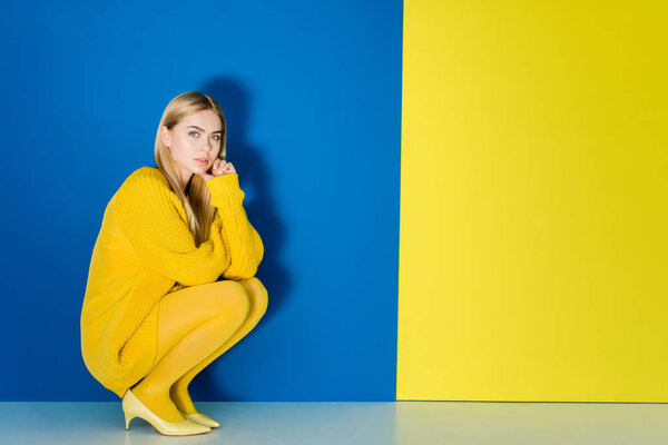 Female fashion model in yellow outfit sitting on blue and yellow background