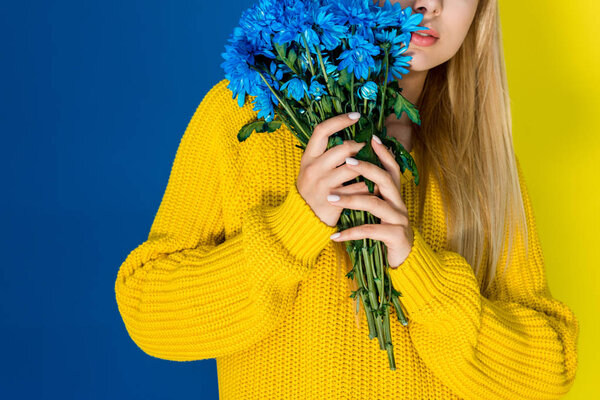 Girl in yellow sweater holding blue flowers isolated on blue and yellow background