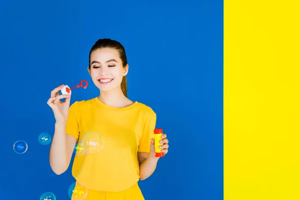 Menina Morena Bonita Soprando Bolhas Isoladas Fundo Azul Amarelo — Fotografia de Stock