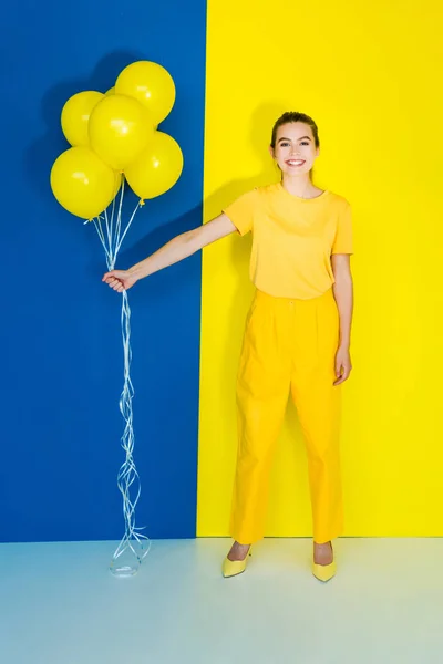 青と黄色の背景に黄色の風船の女性ファッション モデル持株束 — ストック写真