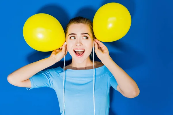 Chica Sorprendida Sosteniendo Globos Por Cabeza Sobre Fondo Azul — Foto de Stock