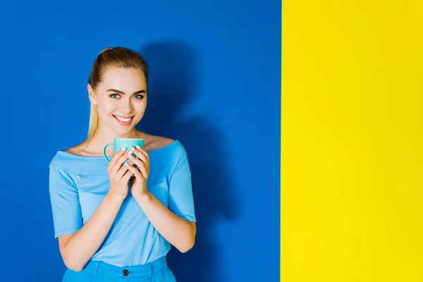 Chica Sonriente Sosteniendo Taza Azul Sobre Fondo Azul Amarillo — Foto de Stock