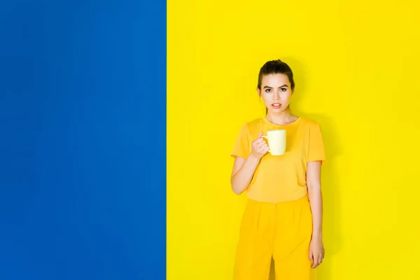 Beautiful Brunette Girl Holding Yellow Cup Blue Yellow Background — Free Stock Photo