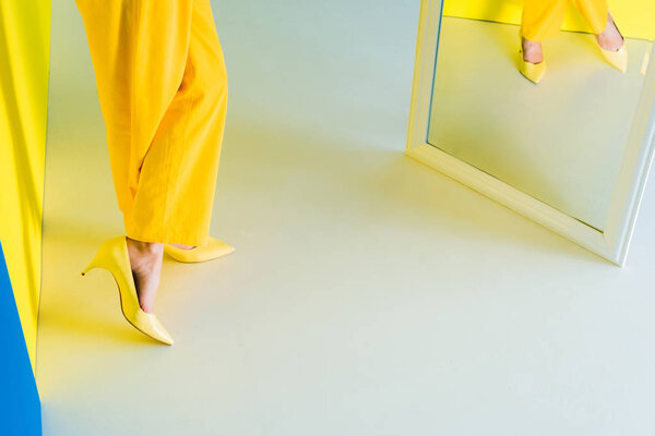 Cropped view of woman in yellow outfit standing in front of mirror on blue and yellow background