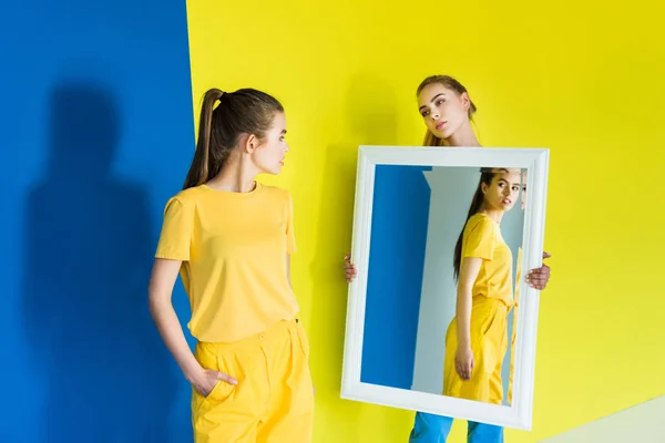 Привлекательная Молодая Девушка Держит Зеркало Своего Друга Синем Желтом Фоне — стоковое фото