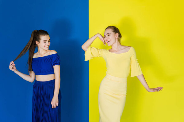 Beautiful brunette and blonde girls in blue and yellow outfits posing on matching backgrounds